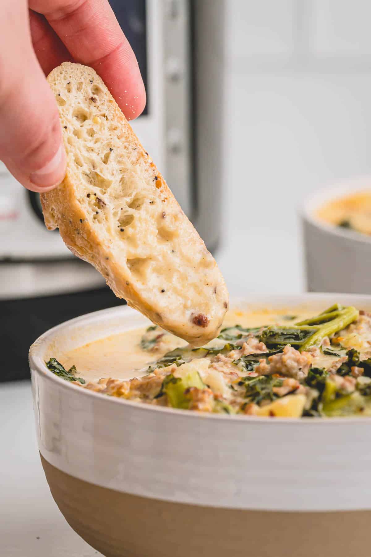 hand dipping crusty bread into soup.