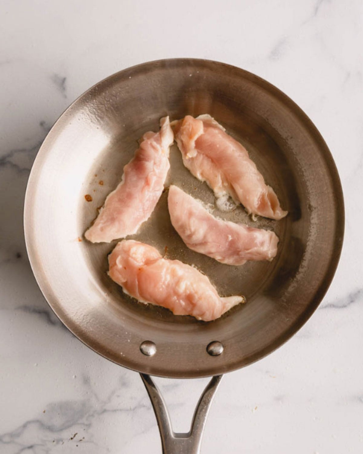 Four chicken tenders in a skillet.