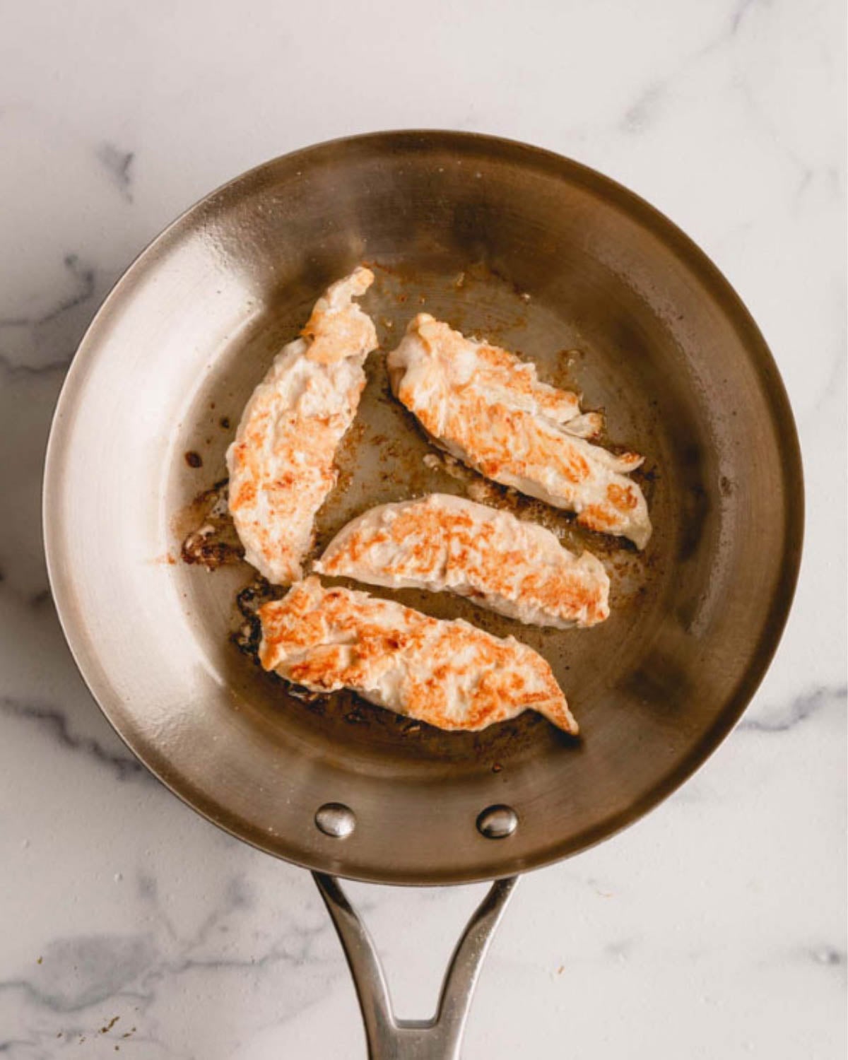 Four chicken tenders in a skillet, flipped.