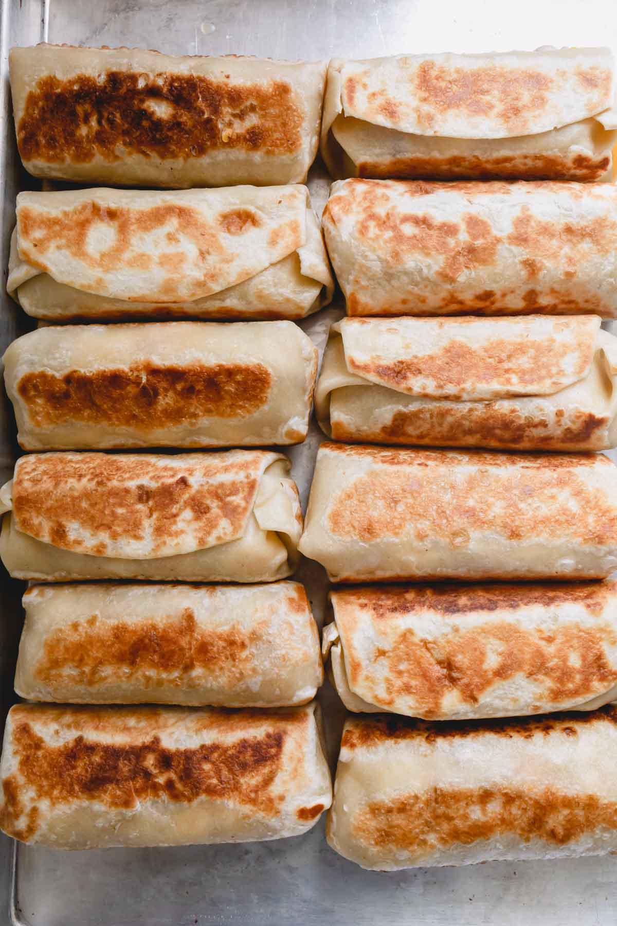 Golden brown breakfast burritos on a sheet pan.