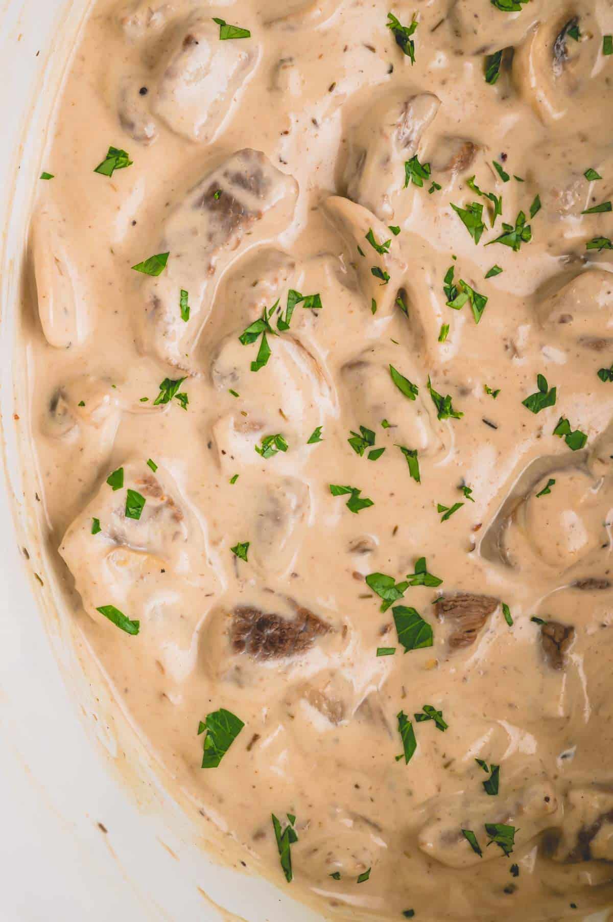 Close up image of beef stroganoff topped with parsley in a slow cooker.