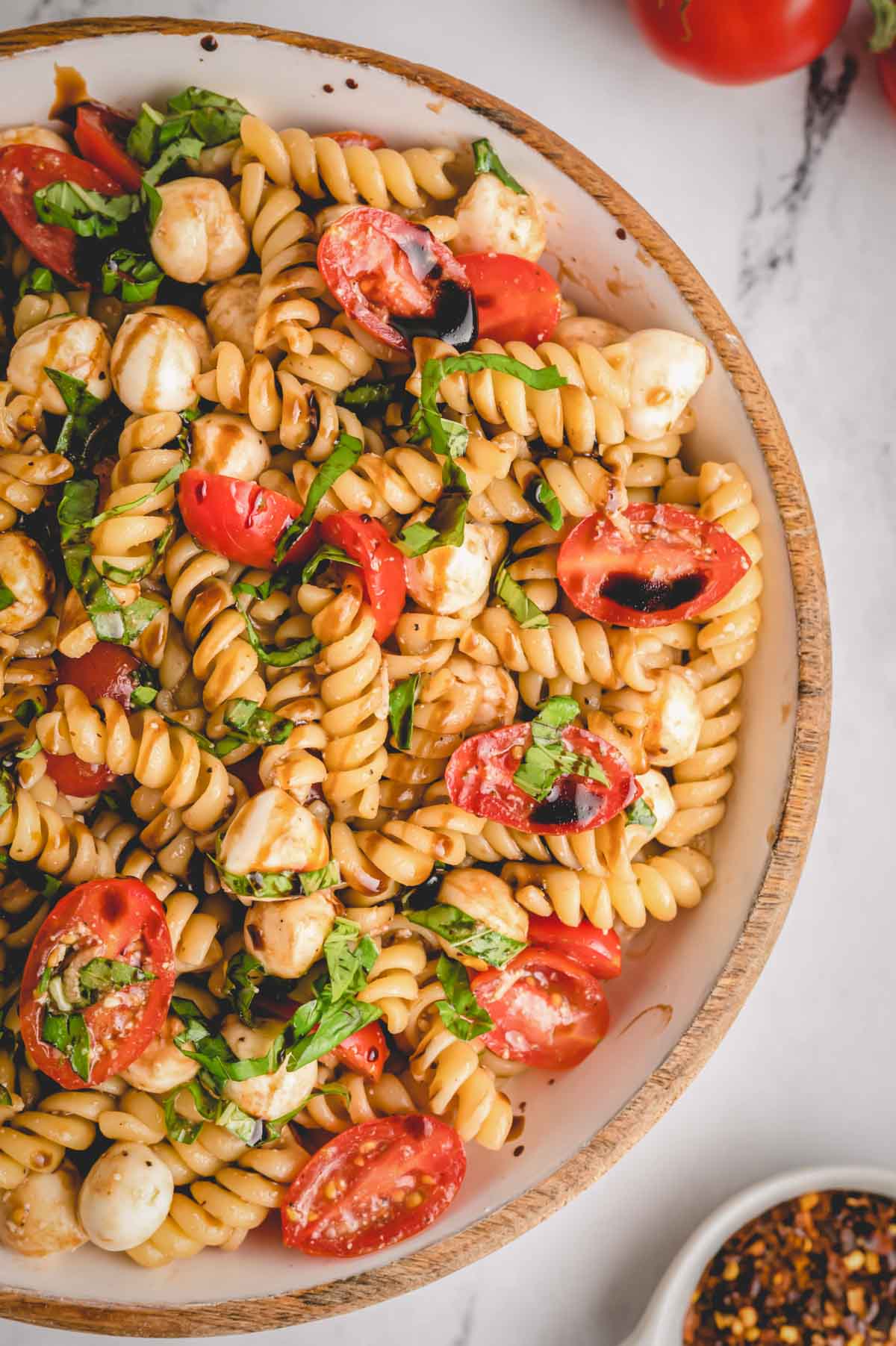 A bowl of Caprese pasta salad topped with fresh basil and balsamic glaze.