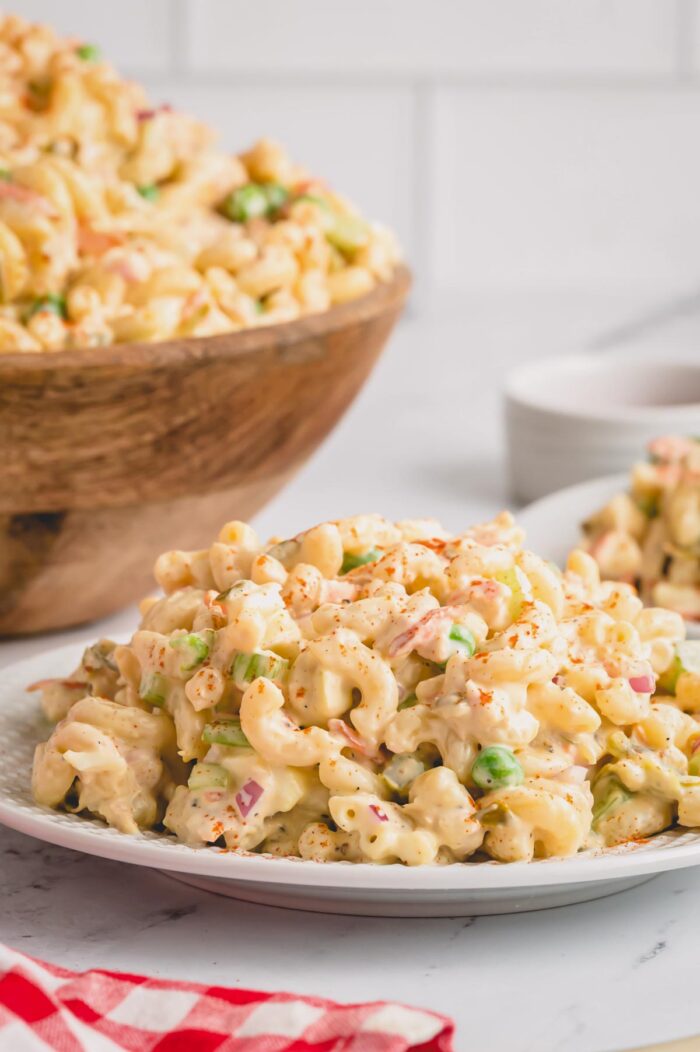 A heaping serving of tuna macaroni salad on a plate with a bowl of the salad in the background.