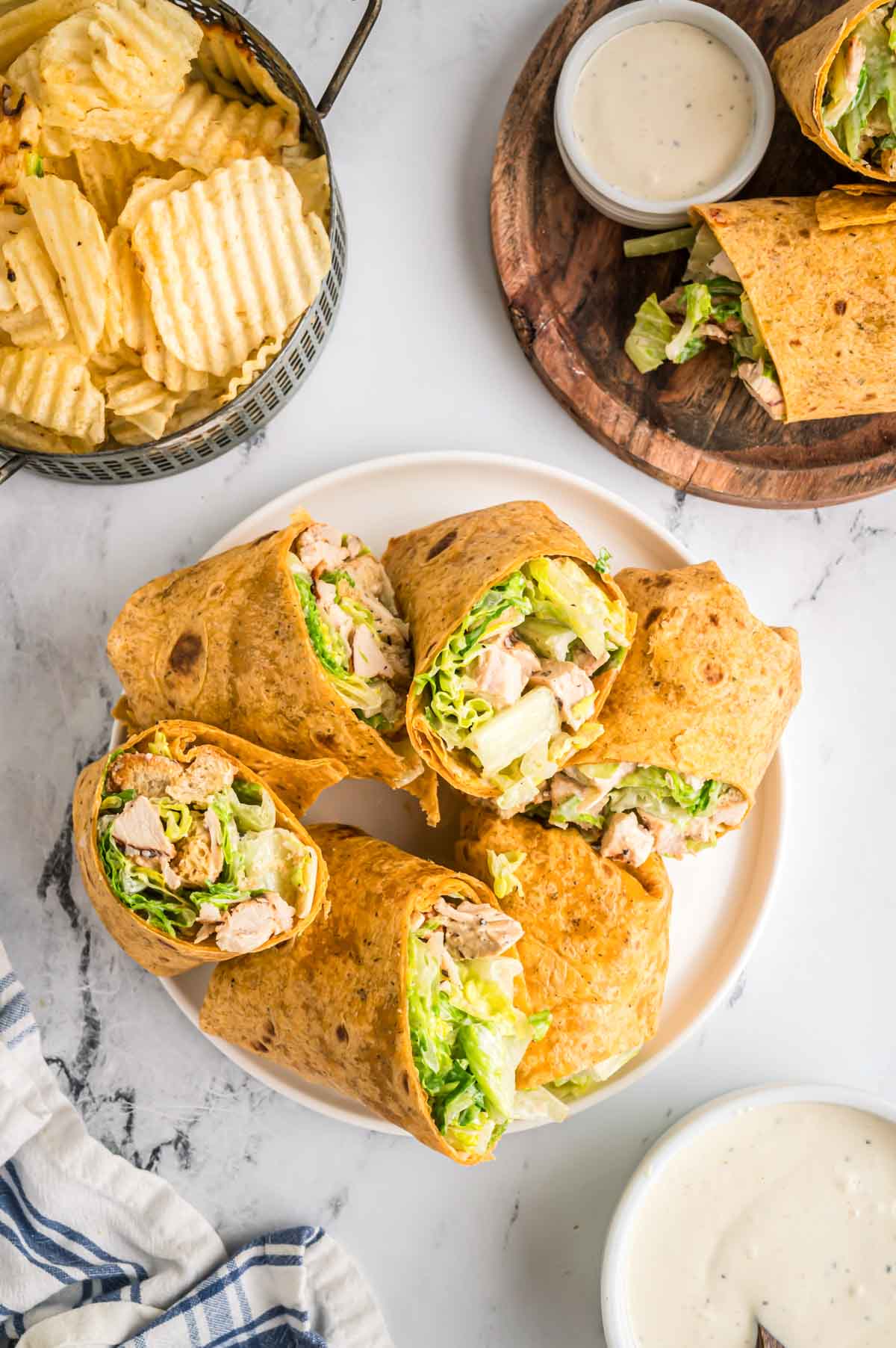 A platter of chicken caesar wraps with chips and caesar dressing on the side.