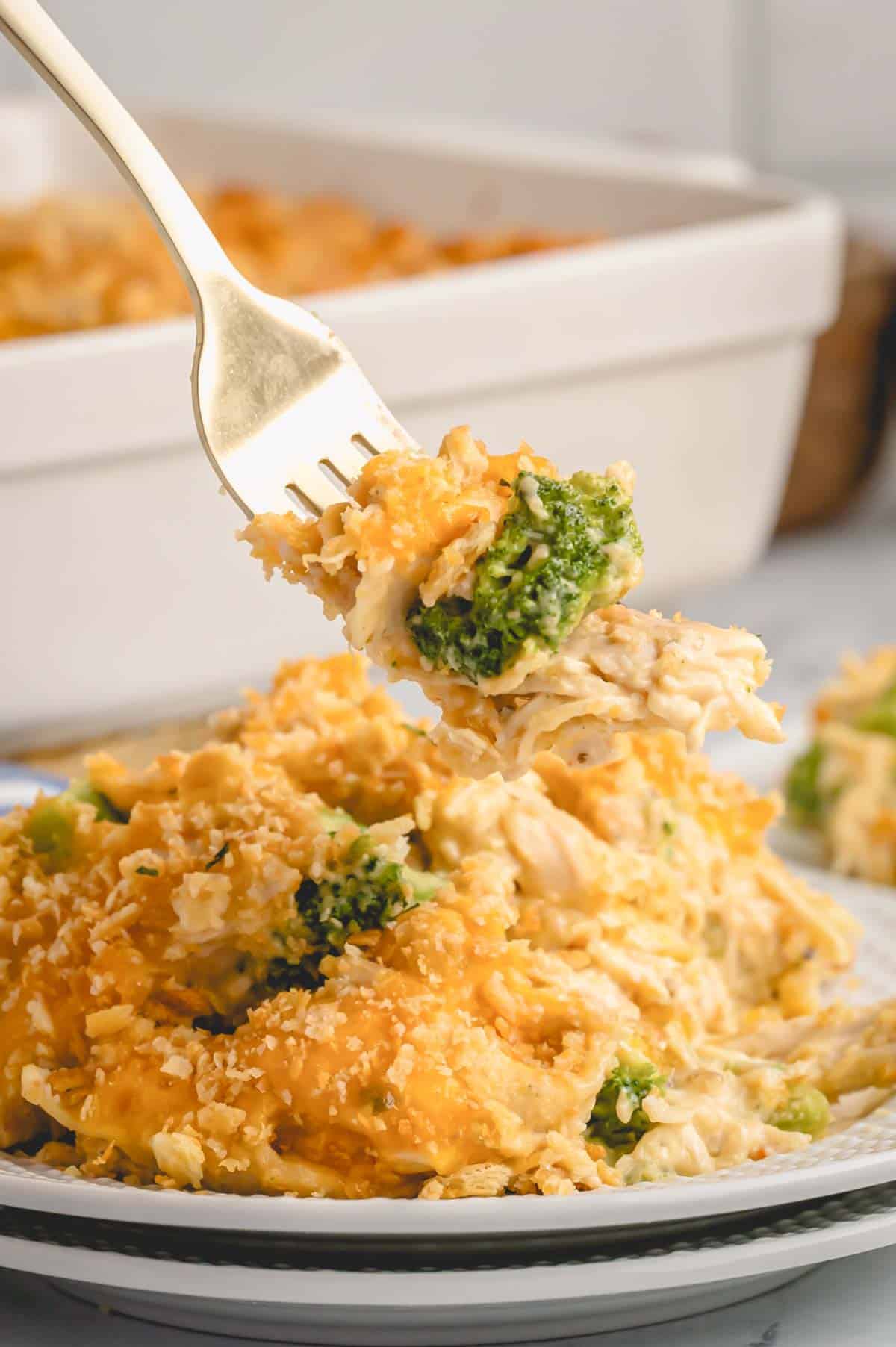 A fork holding a bite of chicken and broccoli casserole over a serving on a plate.