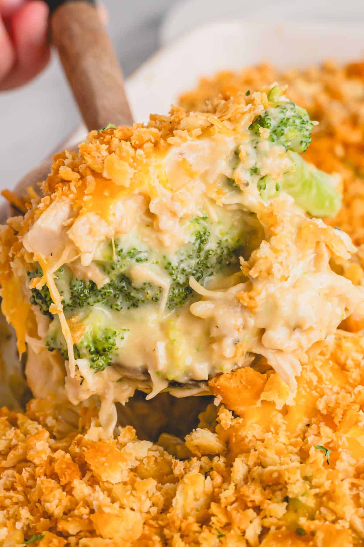 A spoon lifting a scoop of chicken and broccoli casserole from a serving dish.