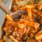 A wooden spoon dipping into a baking dish full of easy baked ziti with sausage.