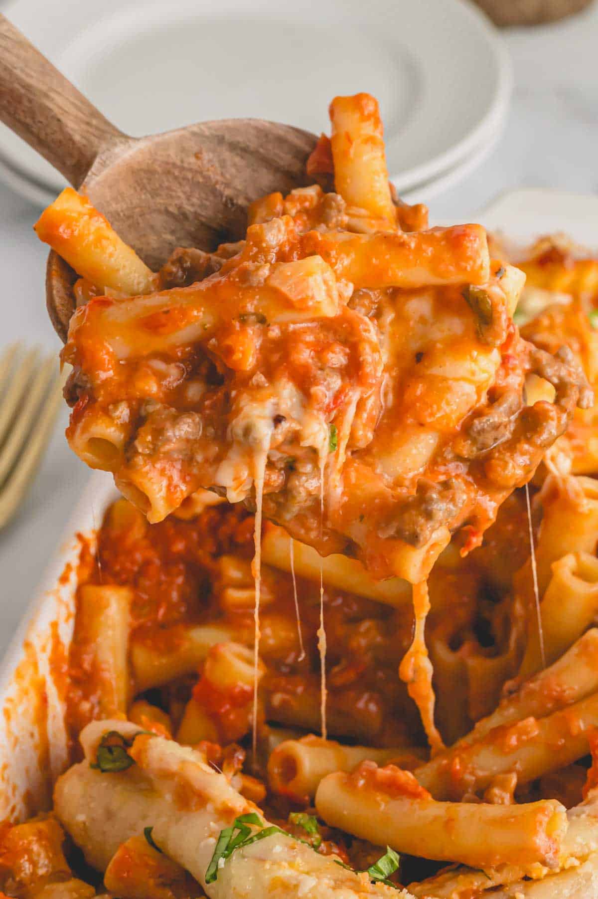 A wooden spoon scooping up a bite of easy baked ziti with sausage.