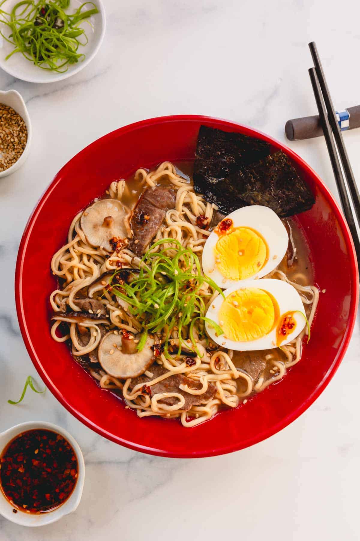 Overhead image of a bowl of ramen with eggs, nori sheets, and scallions.