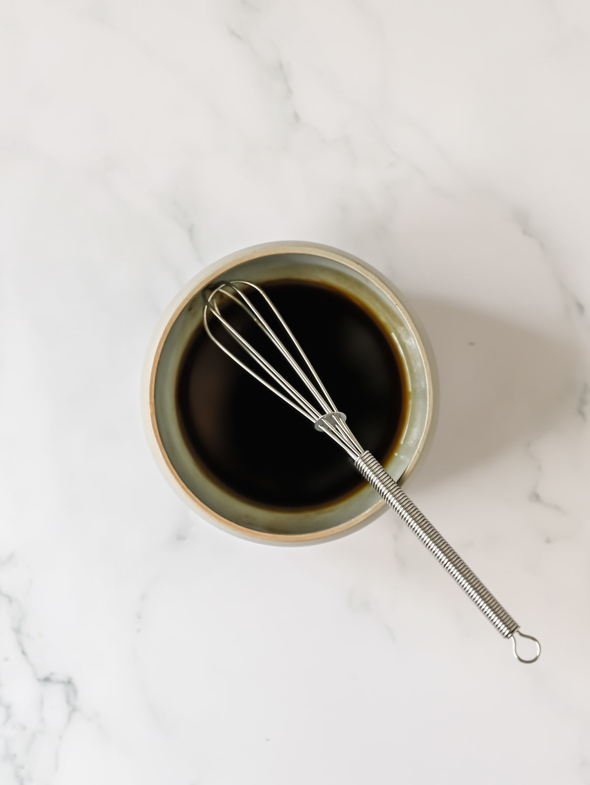 A small bowl of balsamic dressing with a whisk on top.
