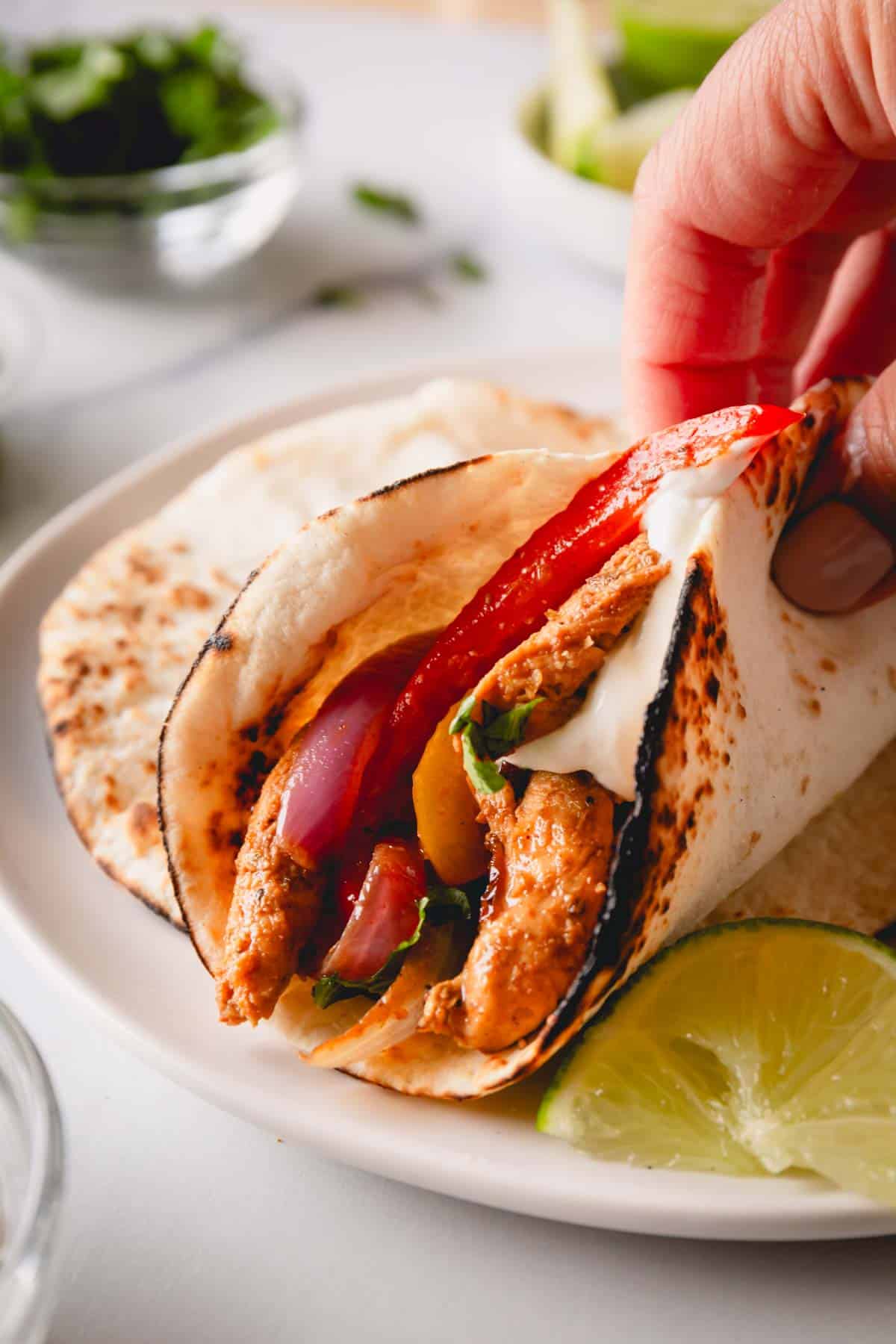 A hand holding a tortilla full of chicken fajitas topped with sour cream.