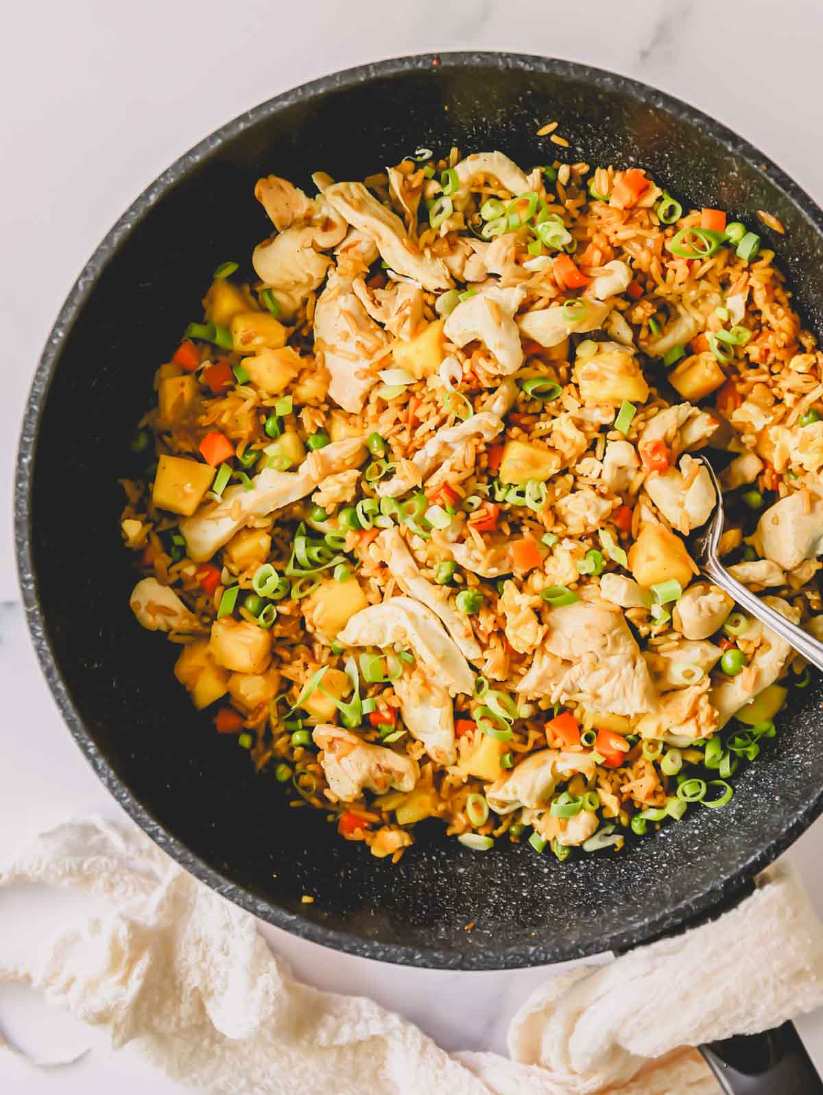 A skillet full of chicken pineapple fried rice with a spoon sticking out.