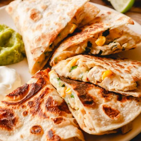 An easy chicken quesadilla on a plate with guacamole and sour cream.