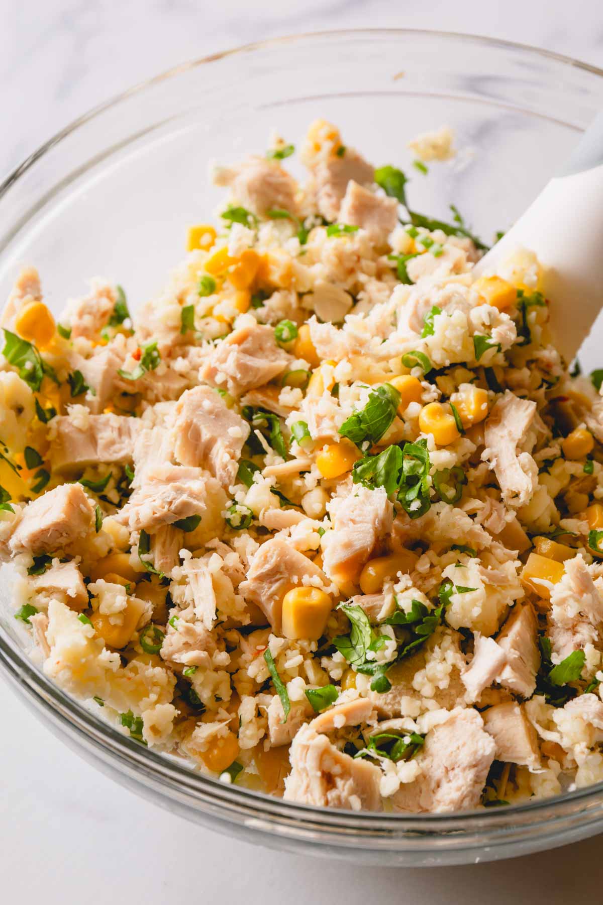 A chicken, rice, corn, and herb mixture being combined in a bowl.