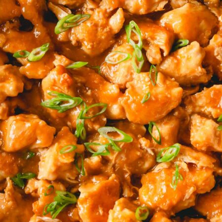 Close up image of homemade orange chicken topped with scallions.