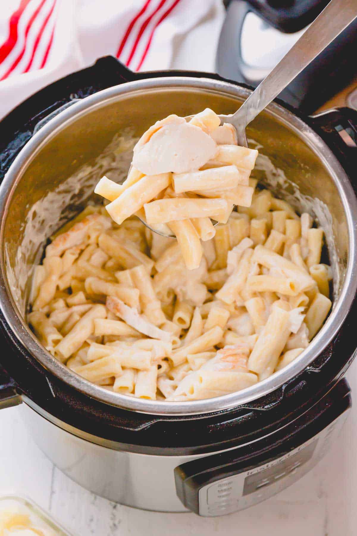 A spoon lifting a scoop of Instant Pot chicken alfredo pasta from the pot.