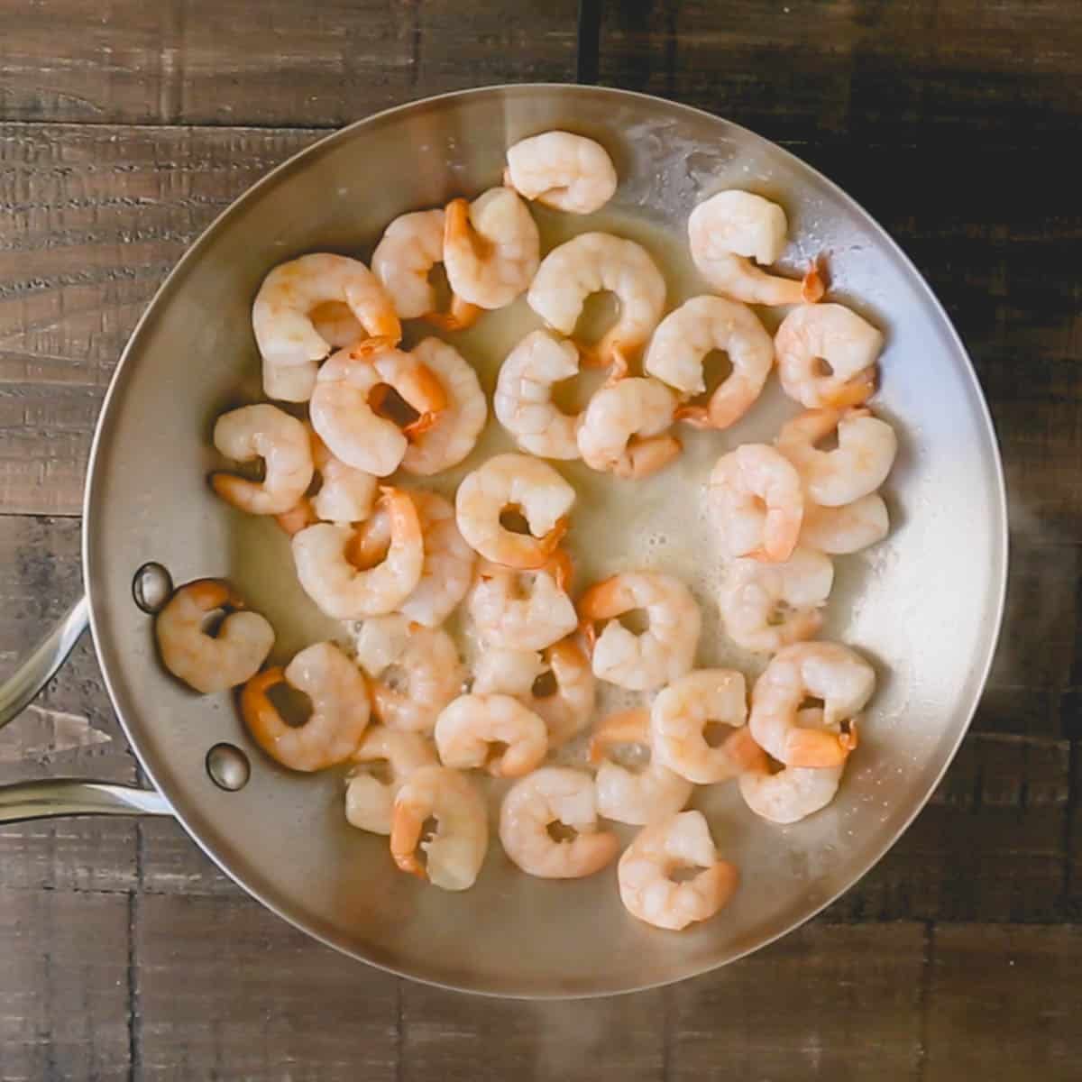 Shrimp are being cooked in a stainless steel skillet.