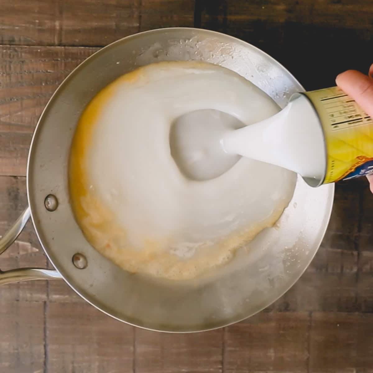 Coconut cream is being poured from a can into an empty skillet.