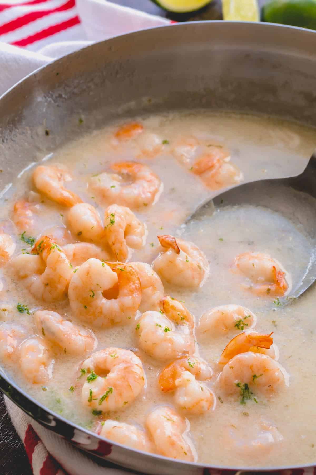 Creamy coconut shrimp in a pan with a ladle scooping up sauce.