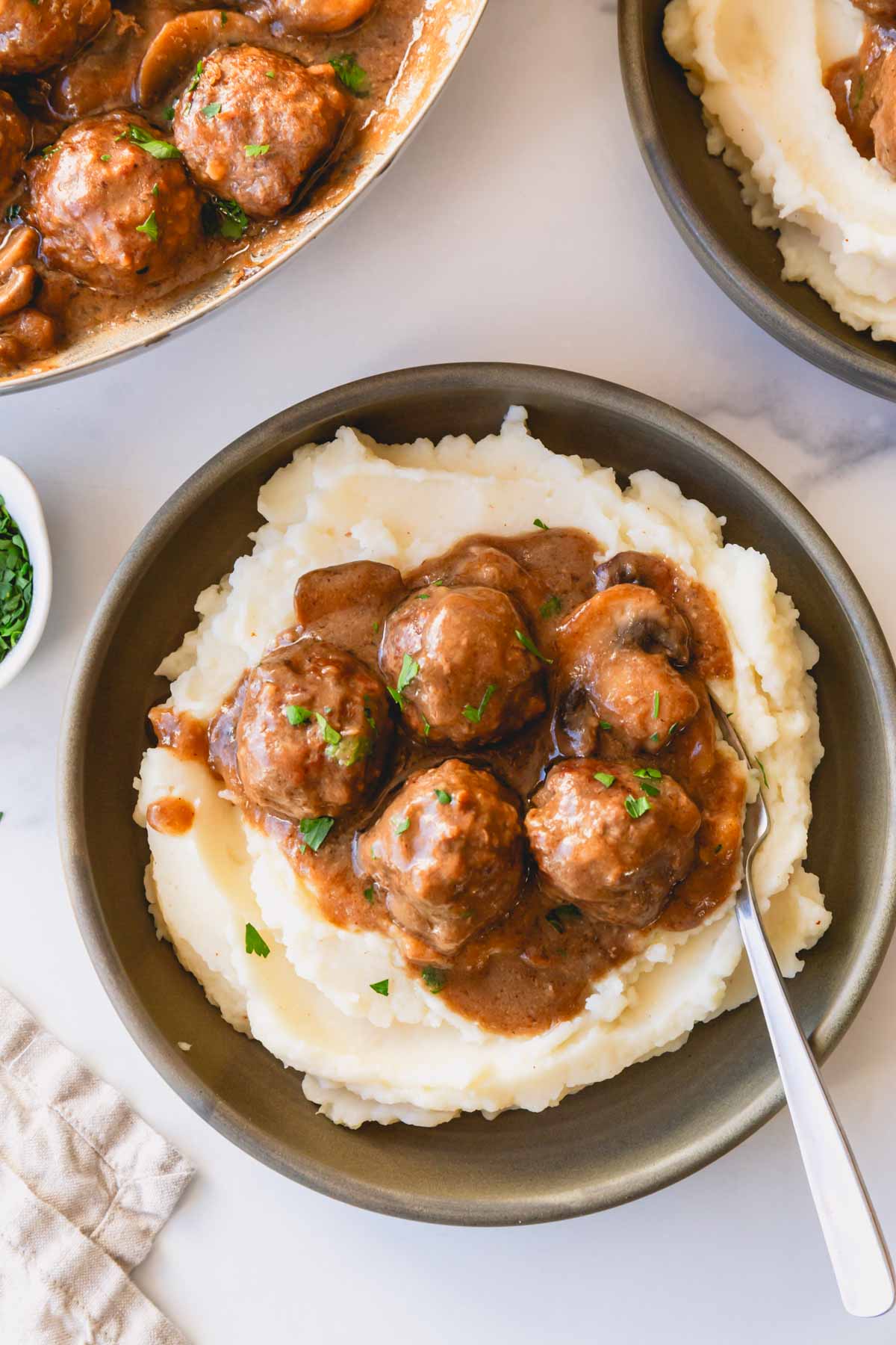 A bowl of mashed potatoes topped with meatballs and gravy with a fork sticking out.