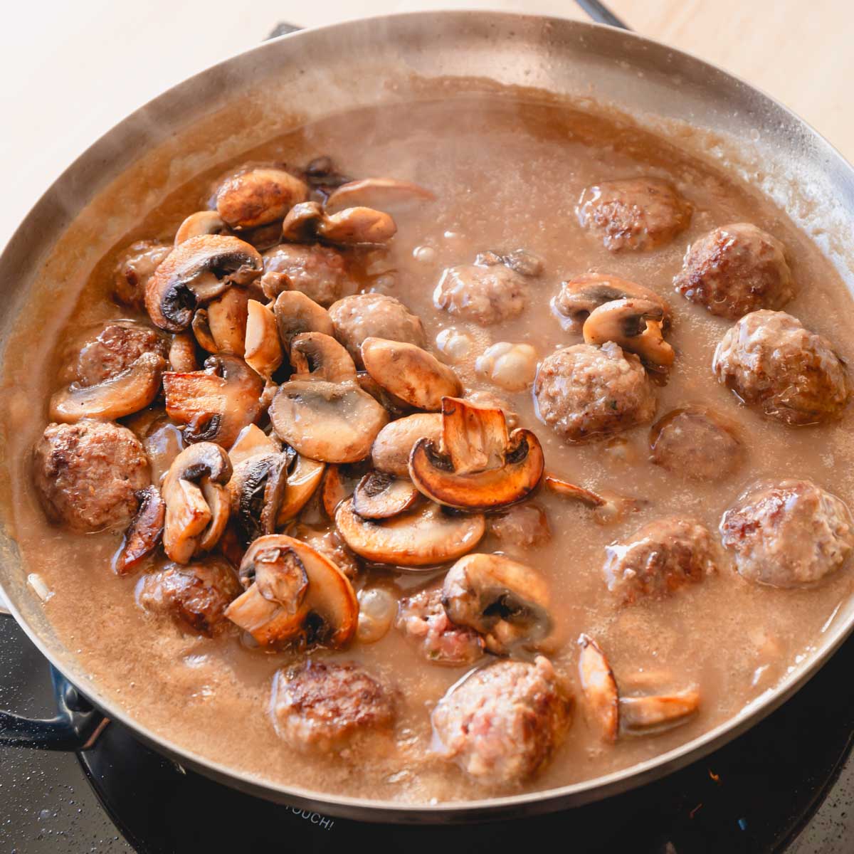 A pan full of mushrooms, meatballs, and gravy.
