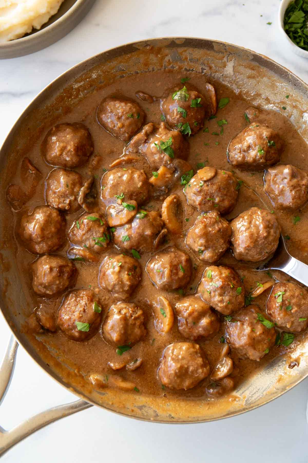 A pan full of meatballs and gravy with a serving spoon lifting a scoop.