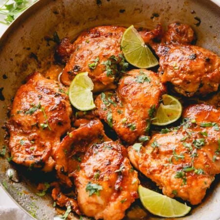 A skillet of cooked cilantro lime chicken thighs topped with lime wedges.