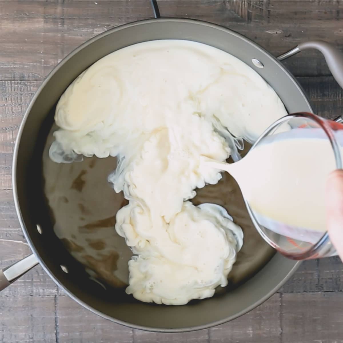 A deep skillet with water and evaporated milk is being poured.