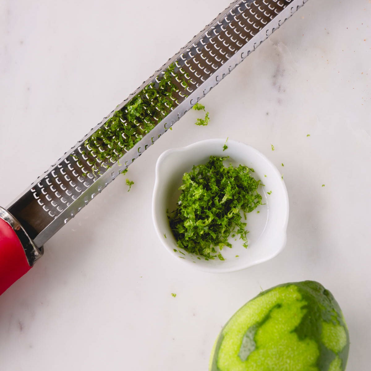 Fresh lime zest with a lime and zester next to it.