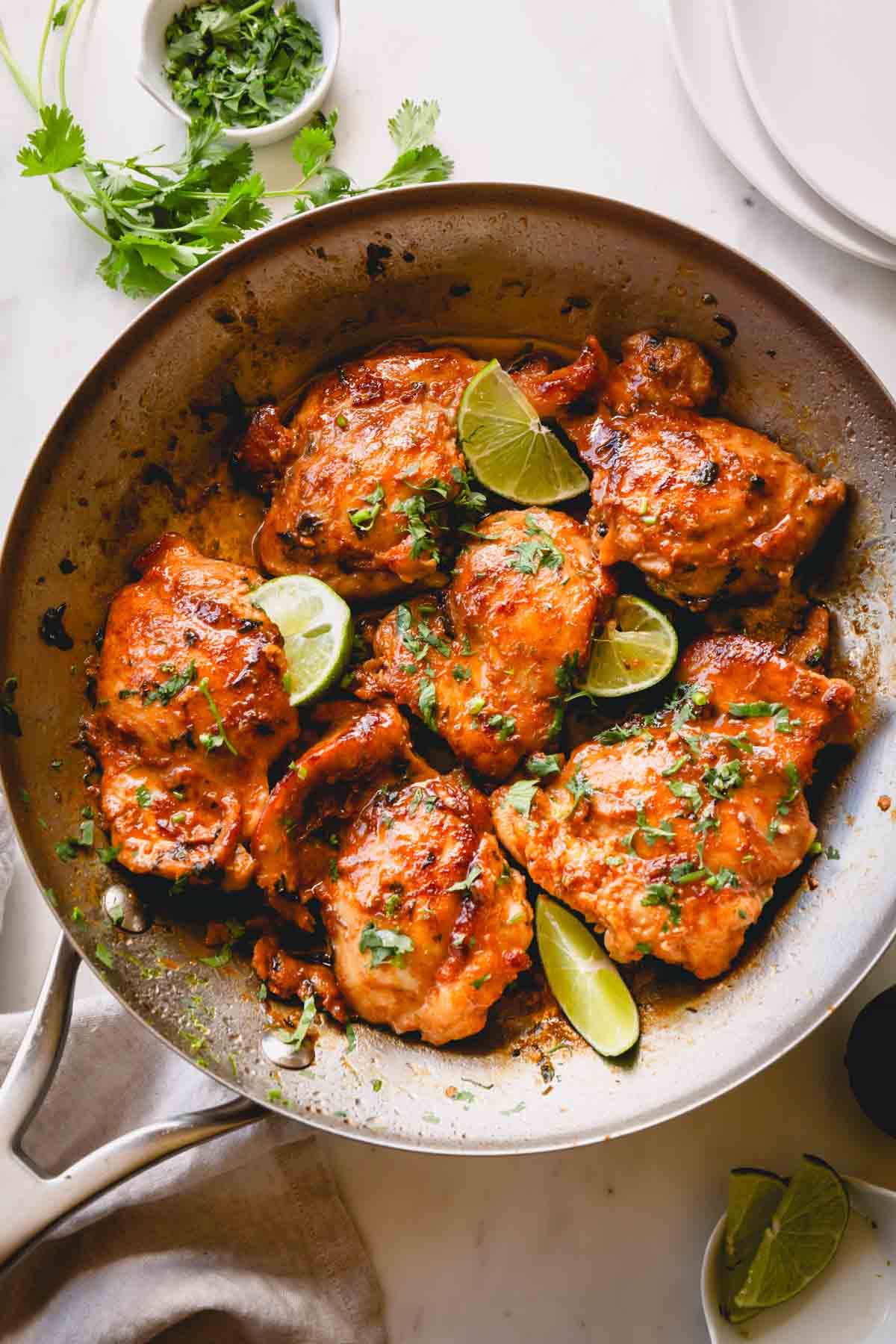 A skillet of cooked cilantro lime chicken thighs topped with lime wedges.