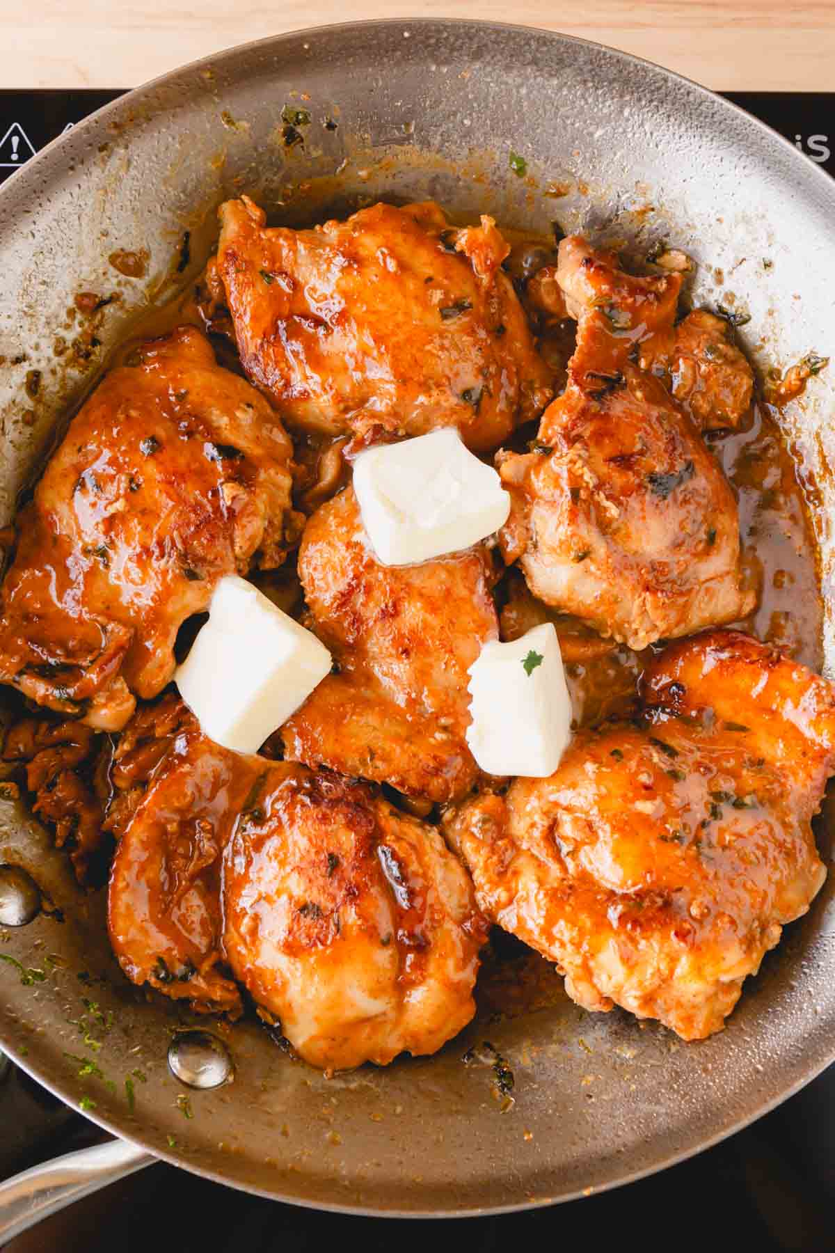 Butter chunks added to the chicken in a skillet.