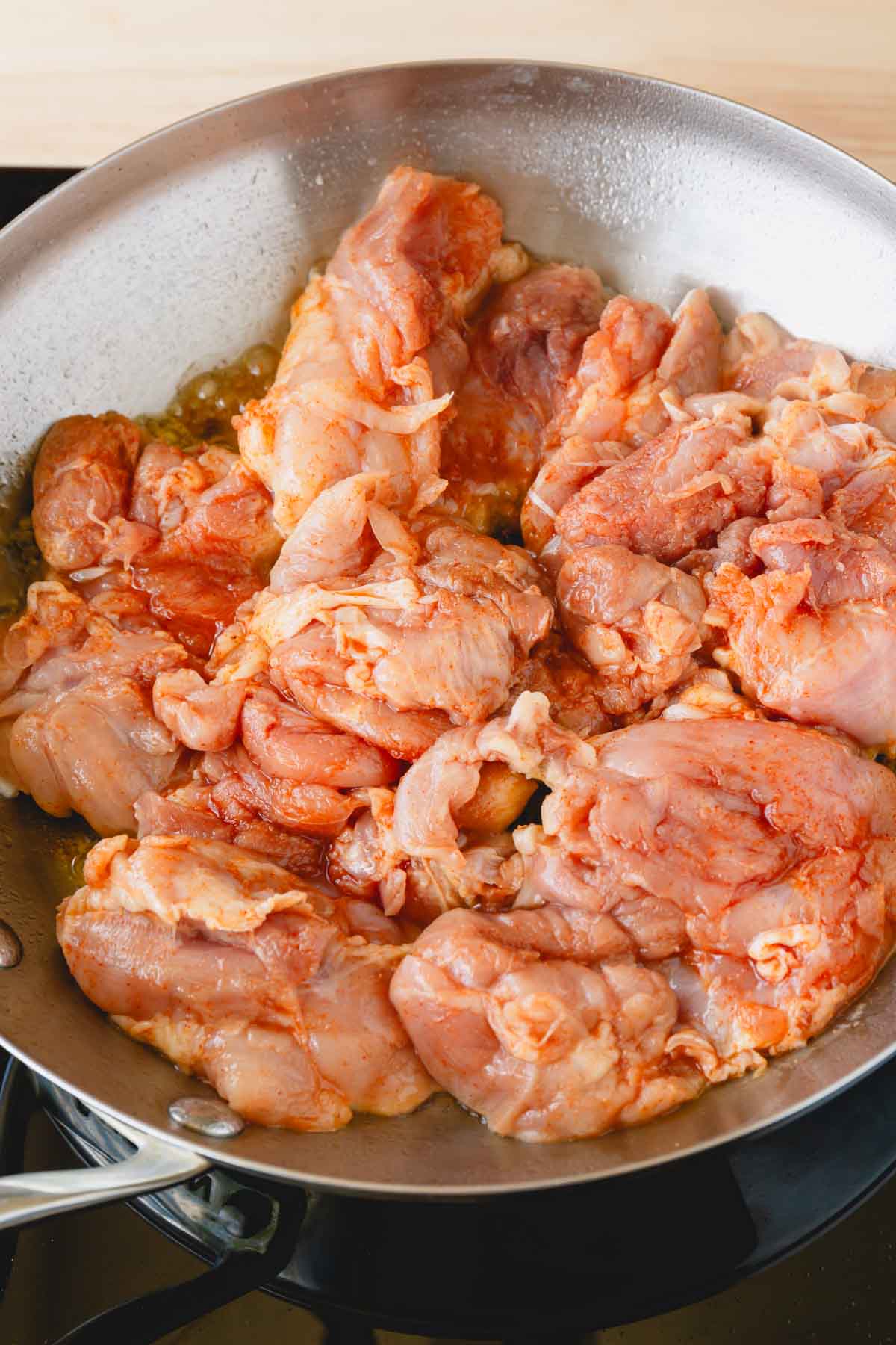 Seasoned chicken thighs in a skillet with a raw side on top.