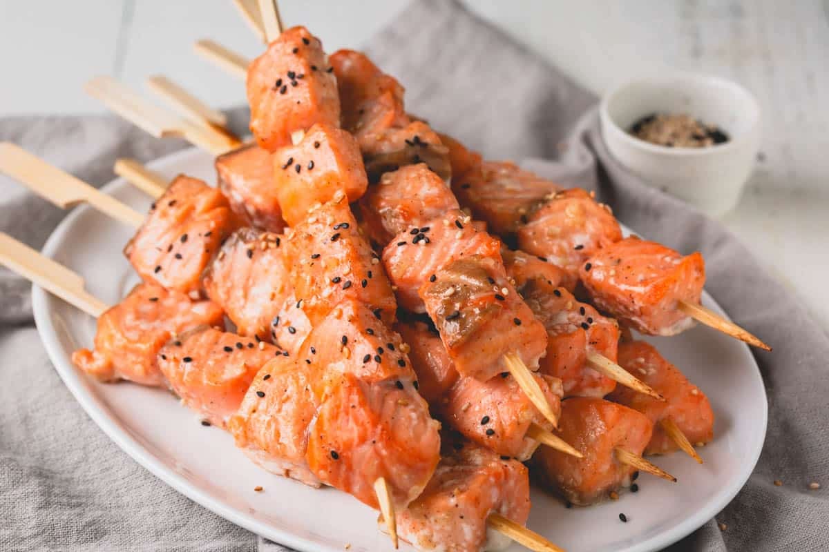 A plate of baked salmon skewers topped with black and white sesame seeds.