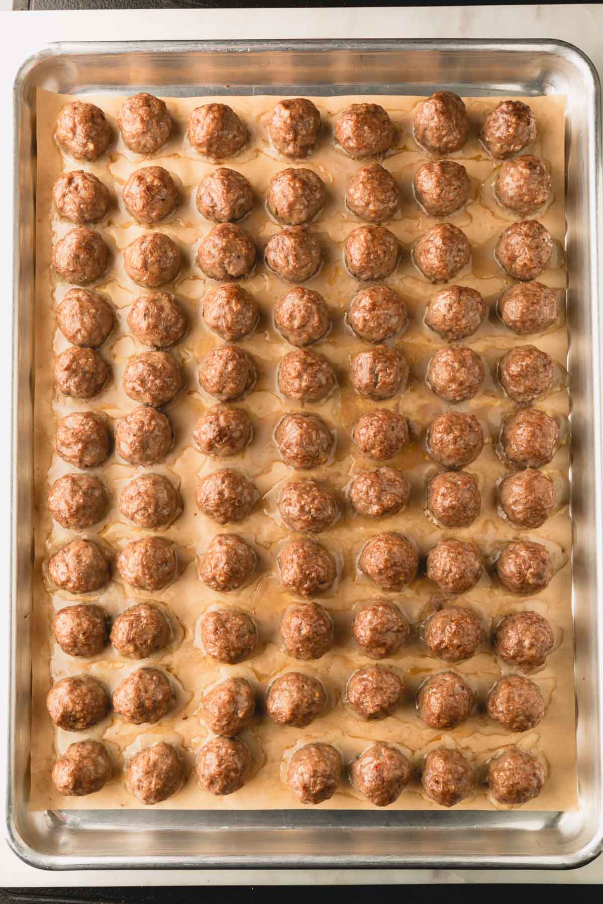 Baked beef meatballs on a parchment paper lined rimmed baking dish.