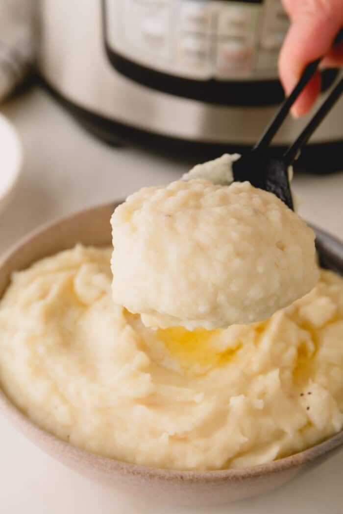 A spoon lifting a scoop of Instant Pot mashed potatoes from a bowl.