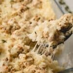 A spoon lifting a scoop of cheesy chicken and rice casserole from a baking dish.