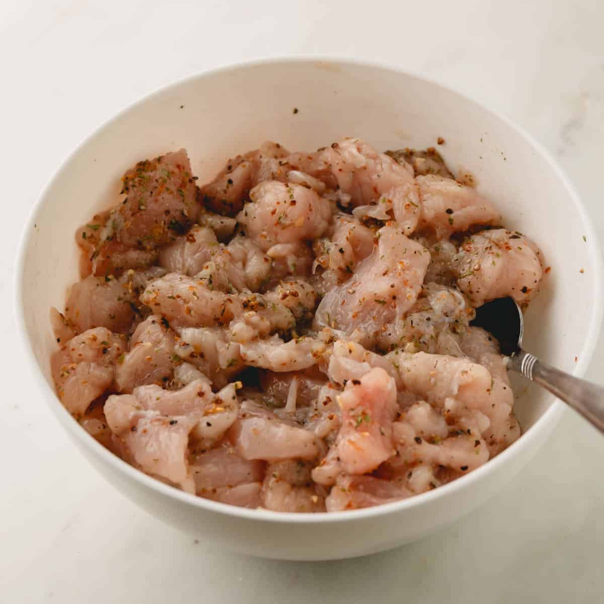A bowl of chicken pieces being tossed with seasonings.