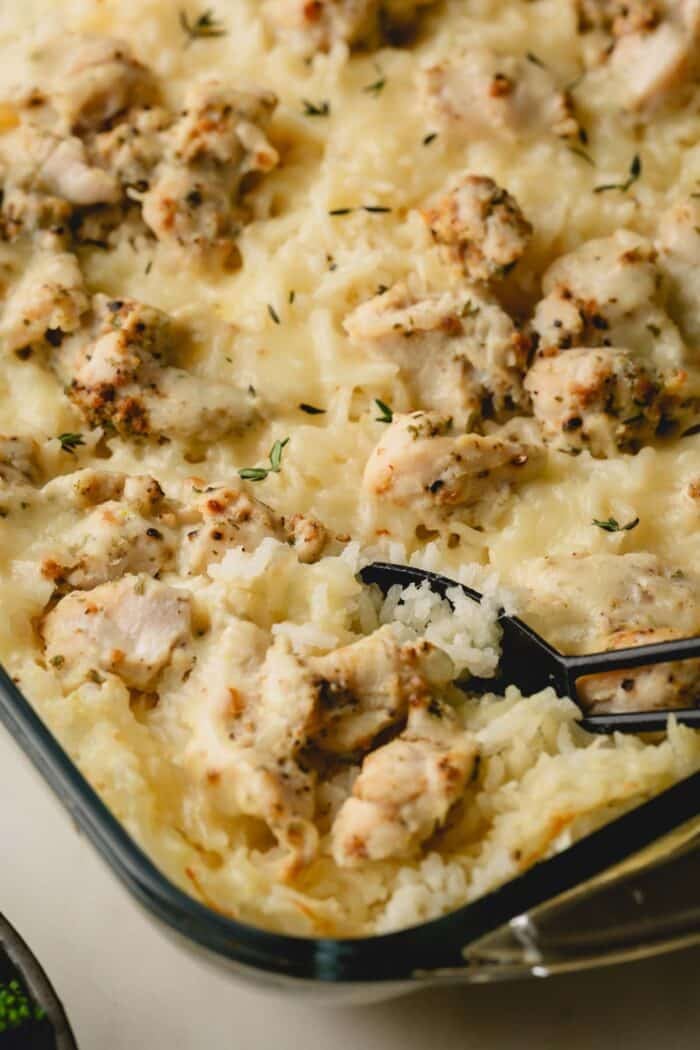 A spoon sinking into a baking dish of cheesy chickan and rice casserole.