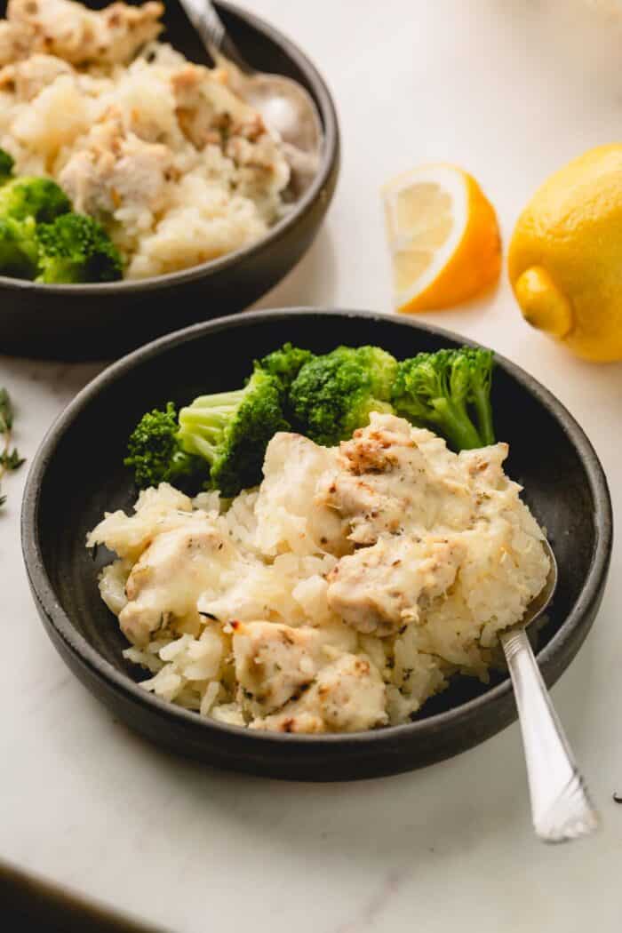 Two bowls of broccoli and cheesy chicken and rice casserole with spoons.