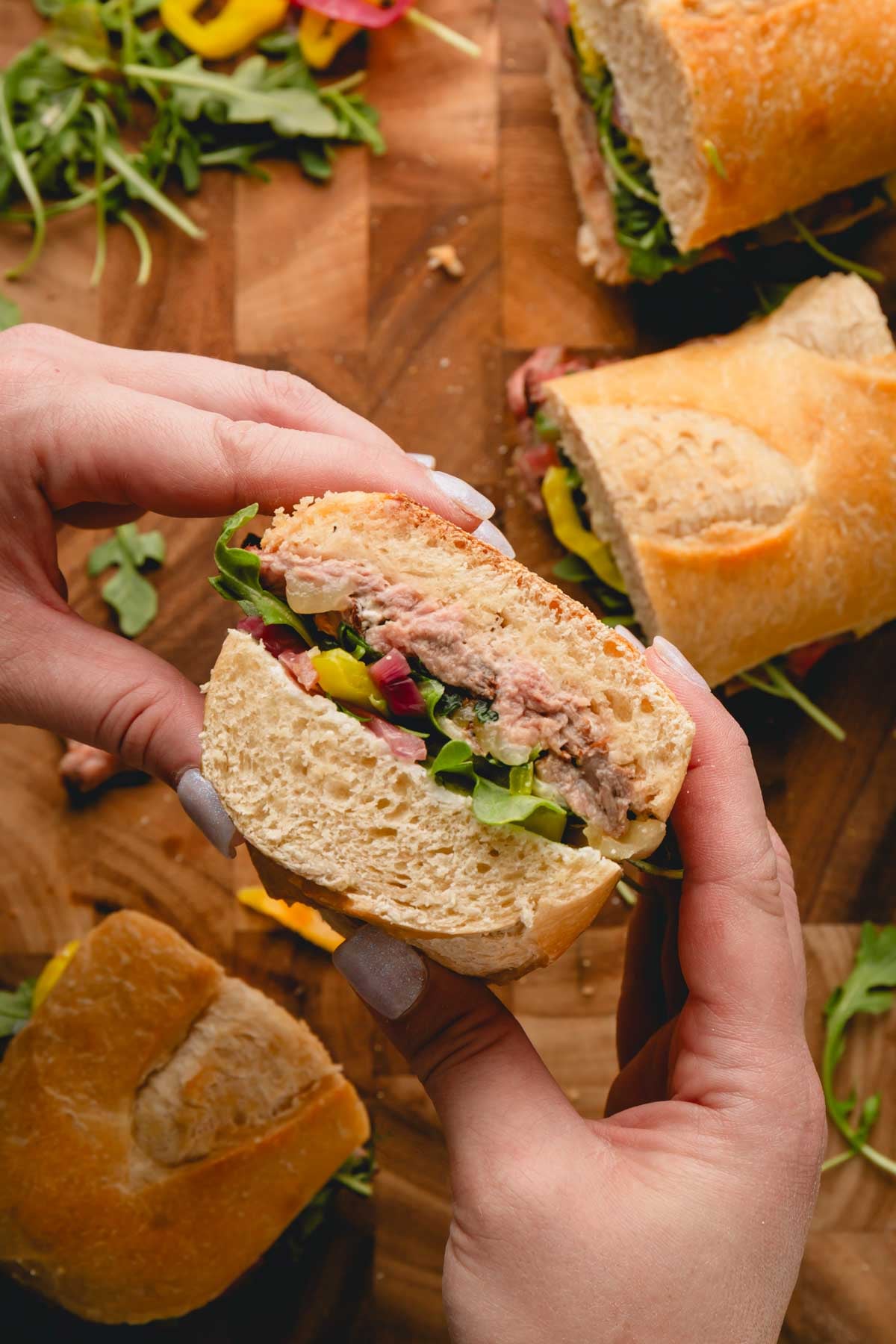 Two hands holding a cheesy ribeye steak sandwich on baguette bread.