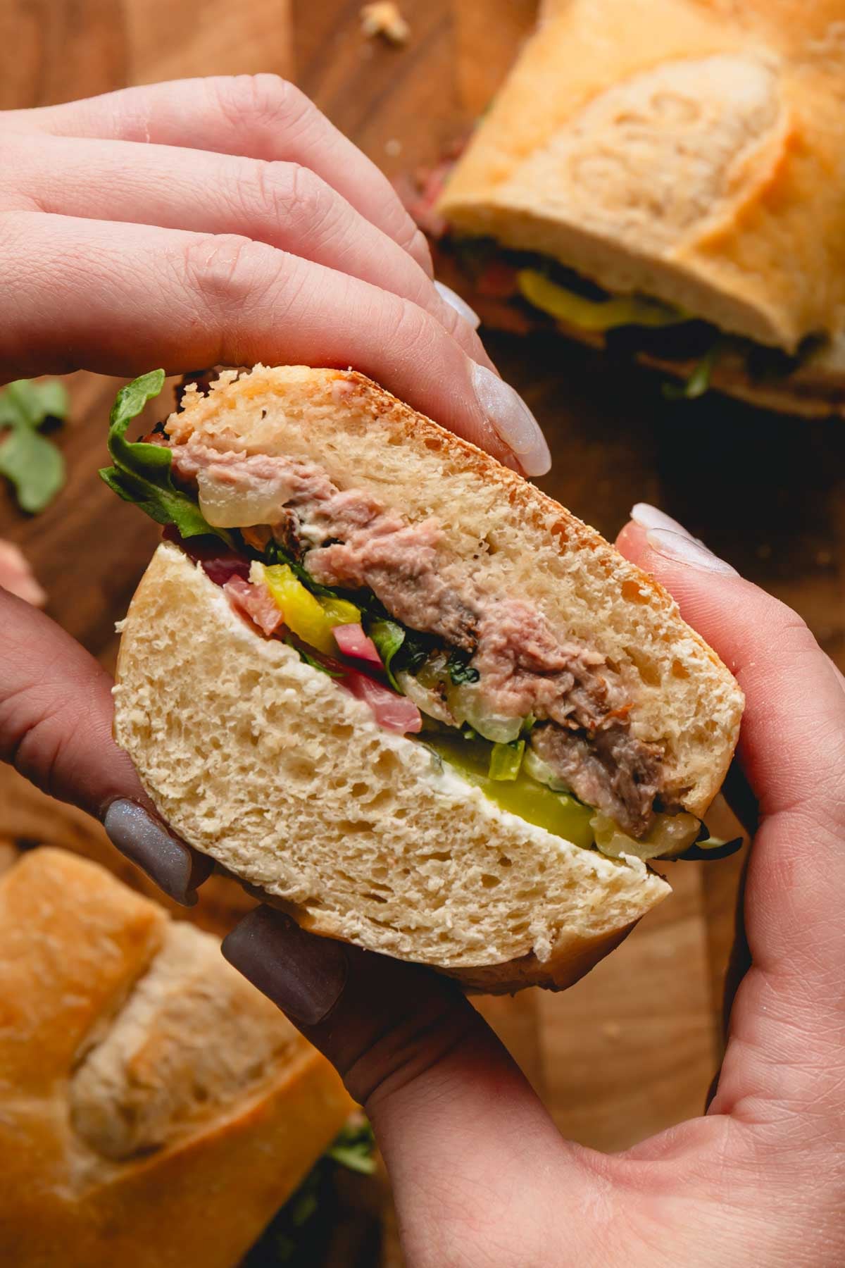 Two hands holding a ribeye steak sandwich.