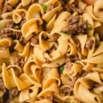 Close up of ground beef and noodles with a wooden spoon.