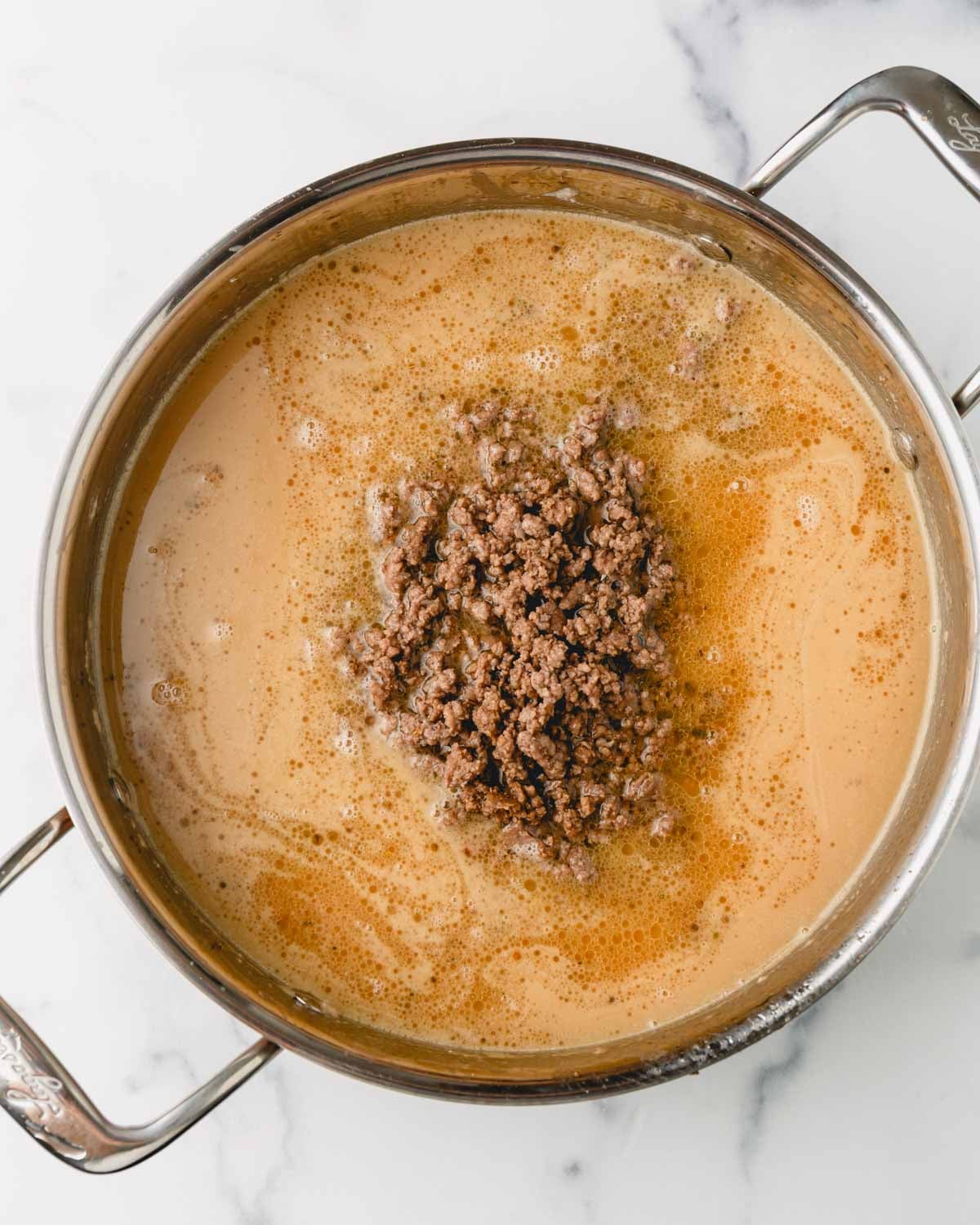 Ground beef is added to the sauce in the large skillet.