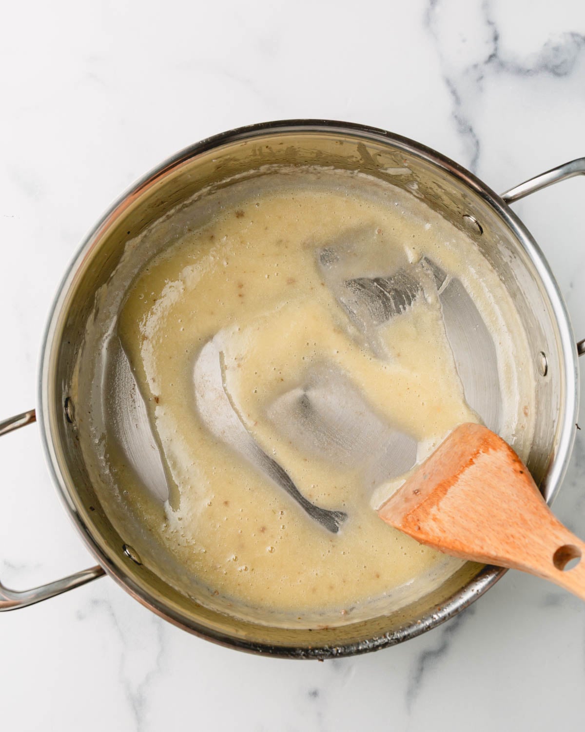 A wooden spoon is mixing the flour and fat in the bottom of the pan.