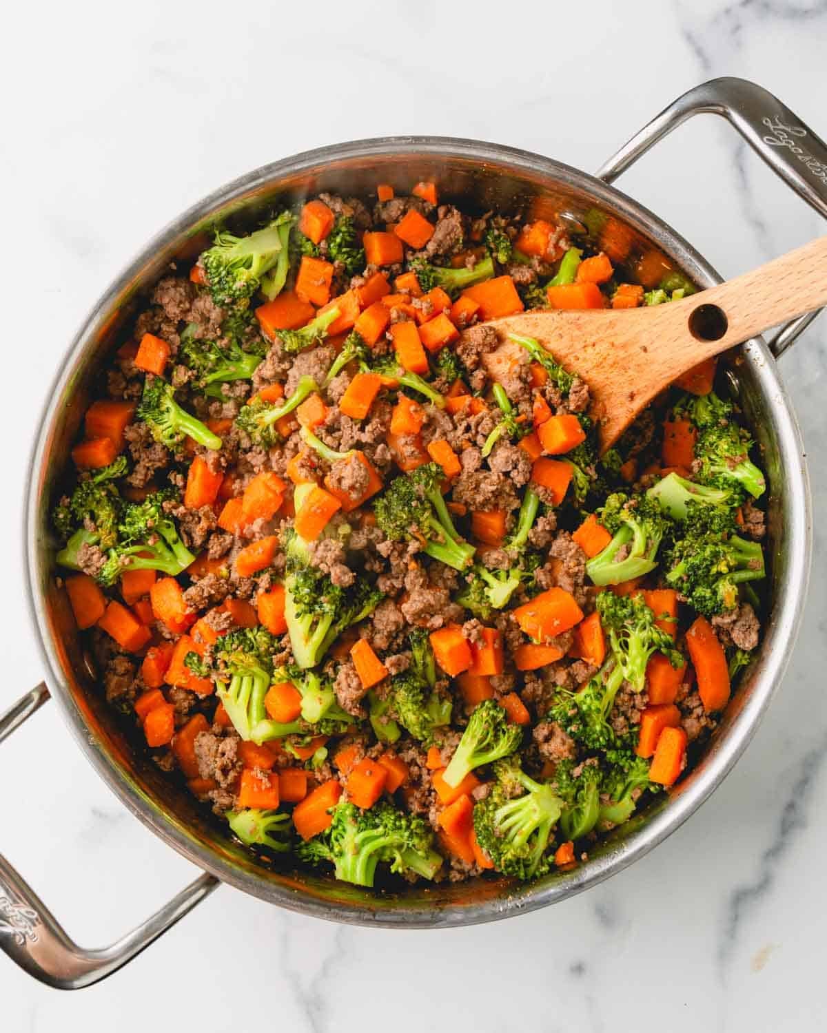 Ground beef, sweet potatoes, and broccoli and cooking in a large skillet with a wooden spoon.
