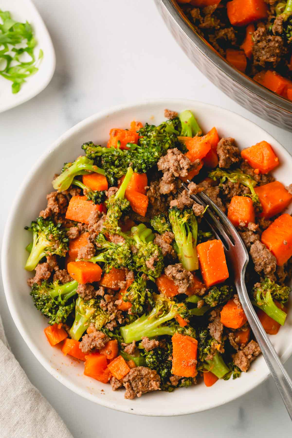 Ground beef and sweet potato skillet is in a white bowl with a fork.