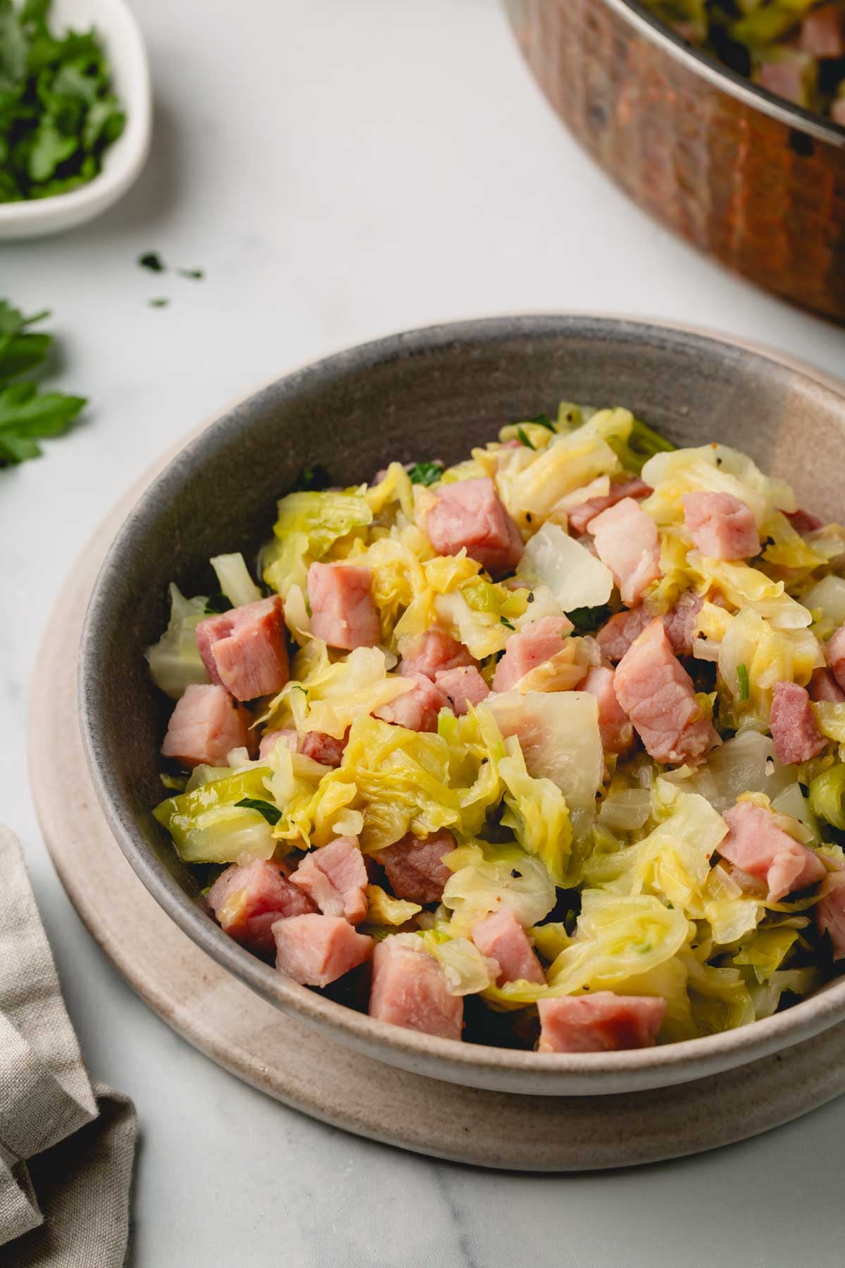 Ham and cabbage is plated in a brown bowl with parsley in the background.