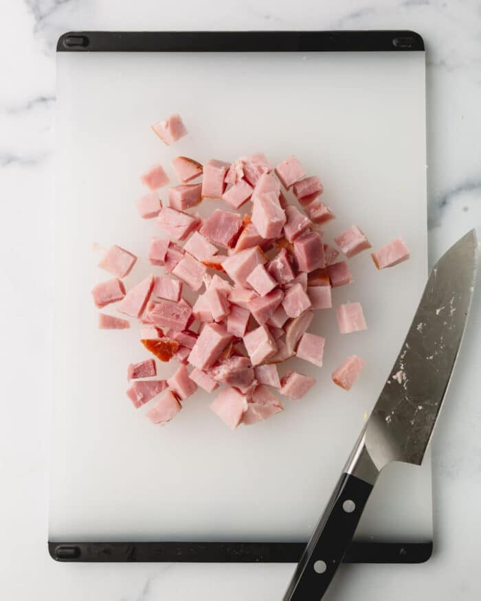 Ham is cubed on a cutting board with a knife.