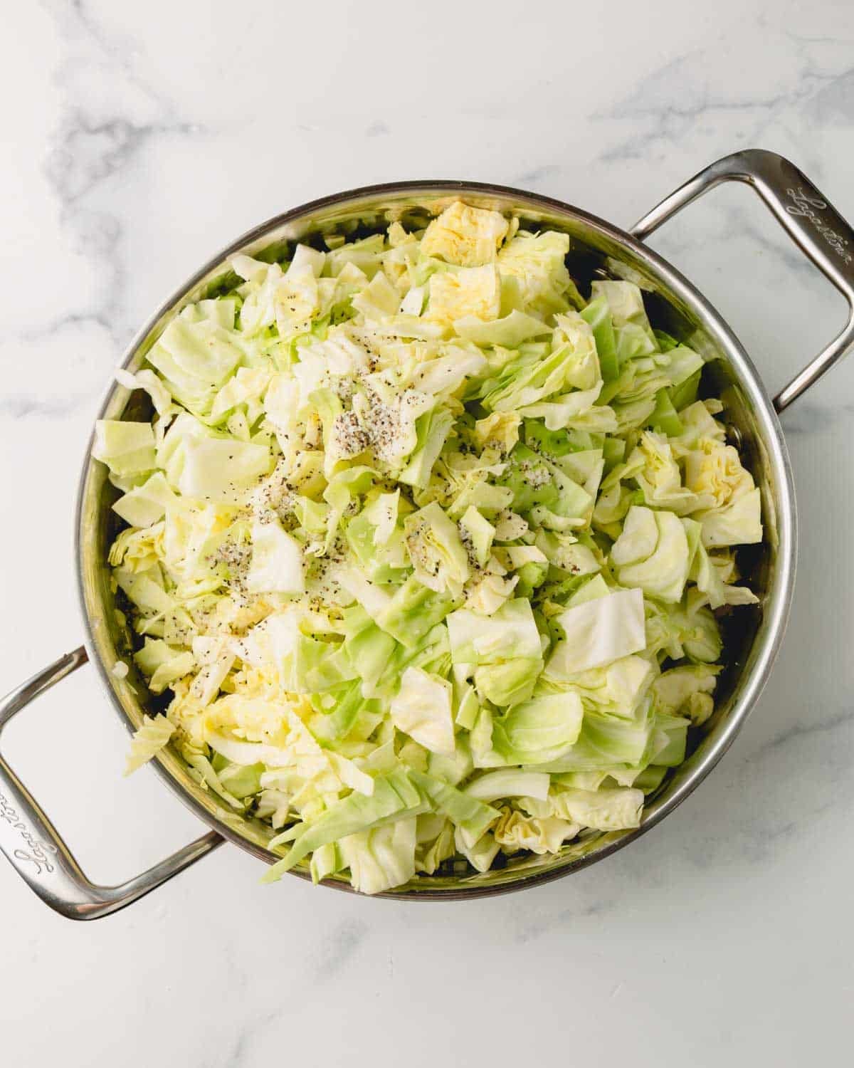 Cabbage, salt, and pepper, are added to the large saute pan.