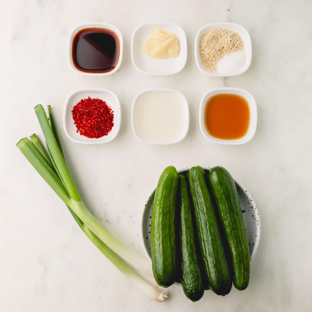 Ingredients for Korean cucumber salad. These include cucumbers, scallions, soy sauce, garlic, sesame seeds, gochugaru, rice vinegar, sesame oil.